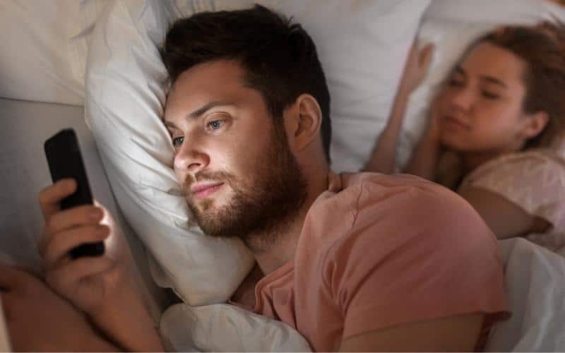 picture of a man texting another woman with his wife sleeping next to him